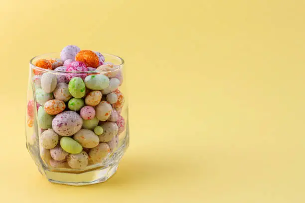 Photo of glass cup with colored candies on a yellow background with a copy of the space