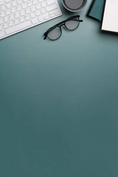 istock Overhead view of designer workplace with keyboard, glasses, notebook a copy space on dark blue background. 1308768192
