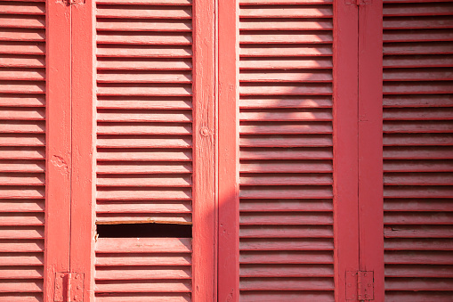 Wooden shutters. Closed, aged, retro red color window shutters for background, texture. Traditional damaged weathered wood structure sunny day,