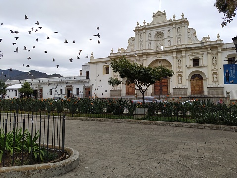 Antigua Guatemala, SA, Guatemala - February 20, 2021: One Saturday in the central park of Antigua Guatemala. The flight of the pigeons and the scampering of the children brightened up that cloudy day. In the background is the San José Cathedral.
