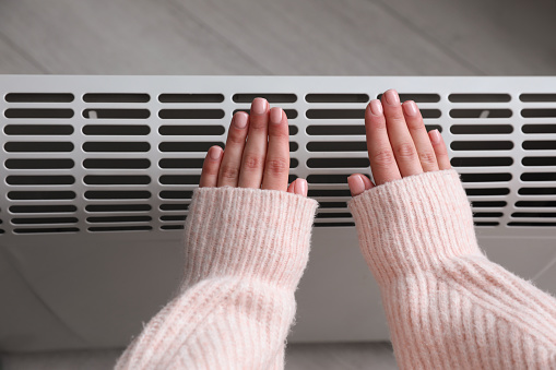 Woman warming hands near electric heater at home,  top view