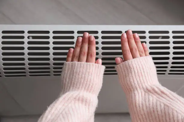 Photo of Woman warming hands near electric heater at home,  top view