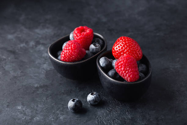 istock Fresh berries in small black bowls on dark stone background 1308791664