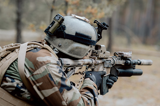 Un soldado con un uniforme militar especial, con un casco en la cabeza y con un rifle de francotirador en el bosque, apuntando a través de un alcance photo