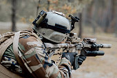 A soldier in a special military uniform, with a helmet on his head and with a sniper rifle in the forest, aiming through a scope