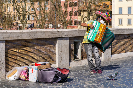 Rome, Italy, March 13 -- A likeable and lonely street artist dressed as a Mexican plays the accordion on the ancient Ponte Sisto in the Trastevere district, protected by a medical mask during the health crisis due to the Covid-19 pandemic. Image in High Definition format.