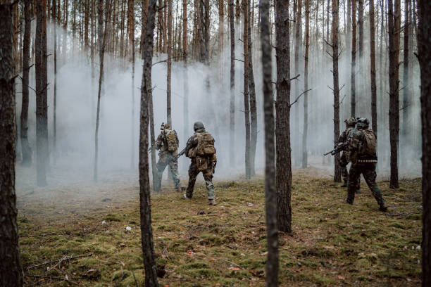 voll ausgerüstete soldaten, die tarnuniform angreifenden feind, gewehre in schussposition. militäreinsatz im einsatz, trupp läuft in formation durch dichten wald am mittag - military training camp stock-fotos und bilder