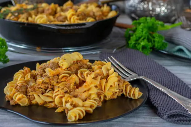 Delicious family meal with minced meat, pasta such as fussily noodles and cabbage served on a plate on wooden table with skillet in the background