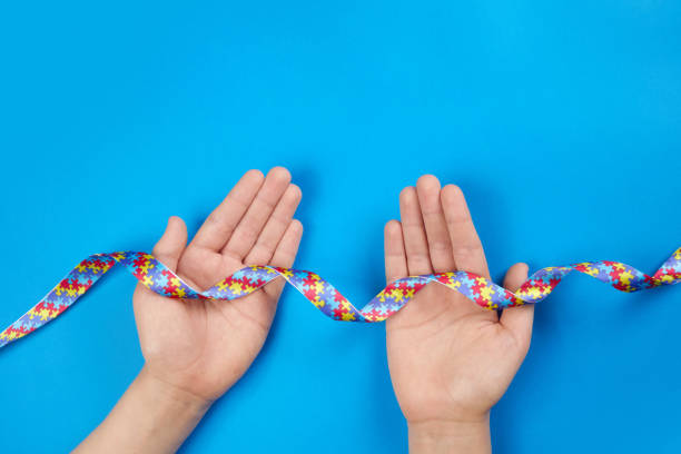 istock World Autism awareness day. Autistic boy hands holding puzzle pattern ribbon on blue background 1308798699