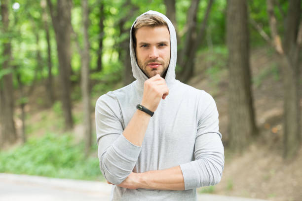 homme barbu dans le capot sur le paysage normal. sportif confiant dans le modèle occasionnel, mode. détendez-vous en forêt ou en parc. prêt pour l’entraînement. entraînement à l’air frais. sport et fitness - hooded shirt men macho hood photos et images de collection