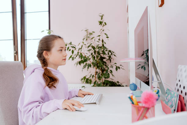 A teenage school-aged girl who uses a desktop computer while sitting at a desk in her room. The young girl is typing on the keyboard and viewing content on monitor. Social distance, remote learning. una adolescente en edad escolar que usa una computadora de escritorio mientras está sentada en un escritorio en su habitación. la joven está escribiendo en el teclado y viendo contenido en el monitor. distancia social, aprendizaje remoto