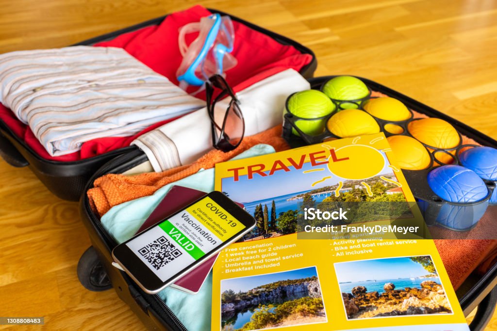 Holiday suitcase with beach travel brochure and mobile phone showing vaccination certificate along with paper passport Suitcase on wooden underground, filled with clothes for tourism. Travel brochure with voucher.
Mobile phone with COVID-19 CoronaVirus vaccination certificate, along with traditional paper passport.

Notes:
- The travel brochure is fake with generic text. It was created by me in photoshop using 3 of my own beach photos.
- The certificate image on the mobile phone is fake and has generic text. It was created by me in photoshop. The QR code decodes as the text: "COVID certificate" Healthy Lifestyle Stock Photo