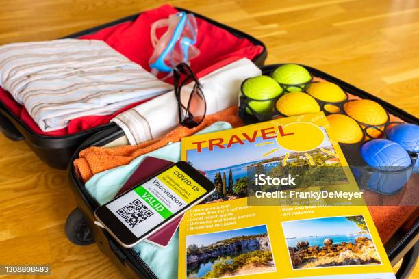 Holiday Suitcase With Beach Travel Brochure And Mobile Phone Showing Vaccination Certificate Along With Paper Passport Stock Photo - Download Image Now