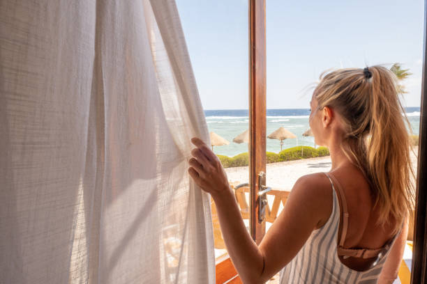 Woman opening curtains in room, morning Waking up in the morning, starting the day right. Sunrise by the beach hotel window view stock pictures, royalty-free photos & images