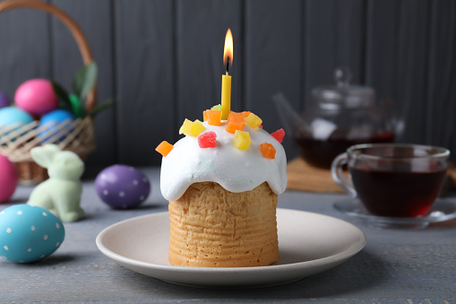 Traditional Easter cake with burning candle on grey wooden table