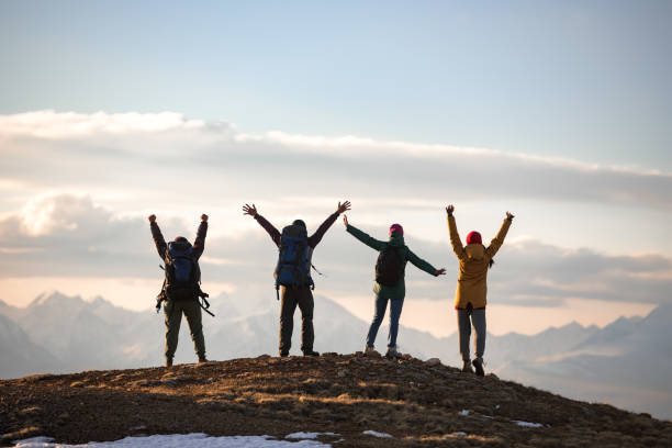Four young tourists with backpacks in winner poses at mountain top Four young tourists are standing with backpacks in winner poses at mountain top altai republic photos stock pictures, royalty-free photos & images