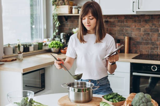 da vicino donna in t-shirt bianca zuppa di cottura con verdure fresche nella cucina loft di casa. menu, banner del ricettario. - mestolo foto e immagini stock