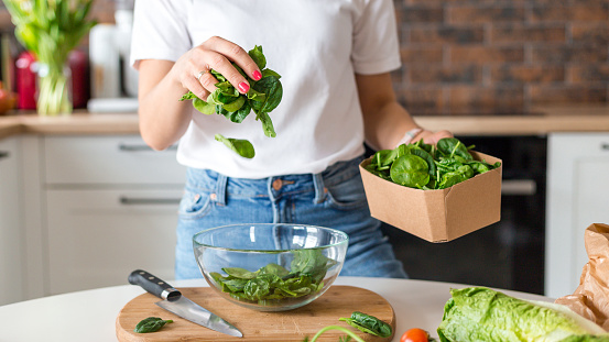 Close up woman in white t-shirt cooking salad with motion effect at home kitchen. Process of cooking healthy food, vegetable concept