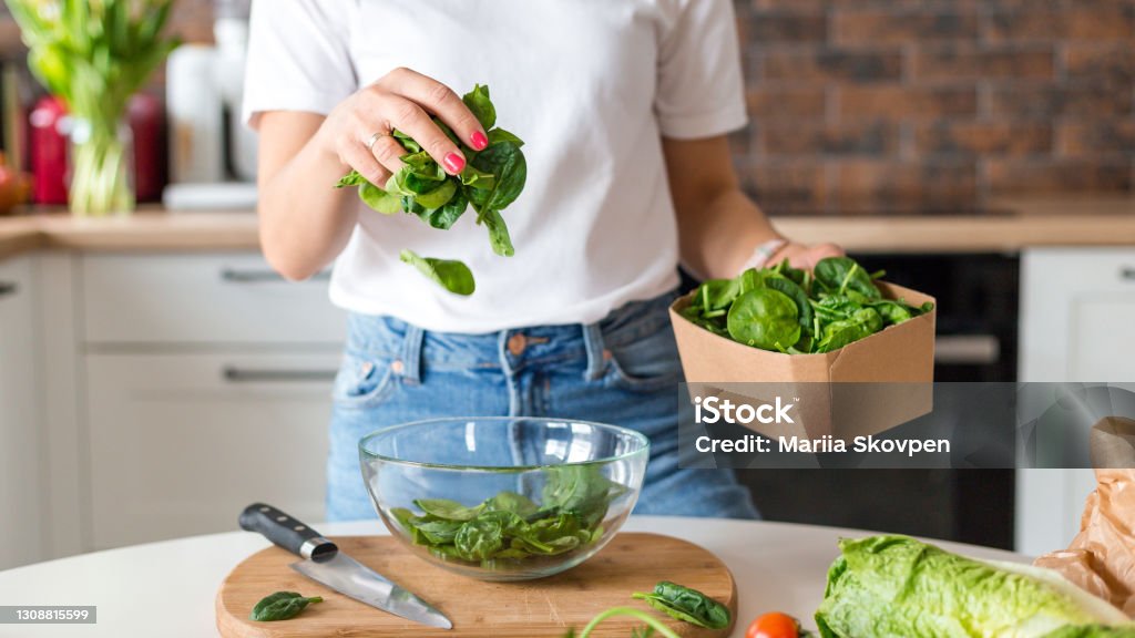 Close up woman in white t-shirt cooking salad with motion effect at home kitchen. Process of cooking healthy food, vegetable salad concept. Menu, recipe book banner Close up woman in white t-shirt cooking salad with motion effect at home kitchen. Process of cooking healthy food, vegetable concept Spinach Stock Photo