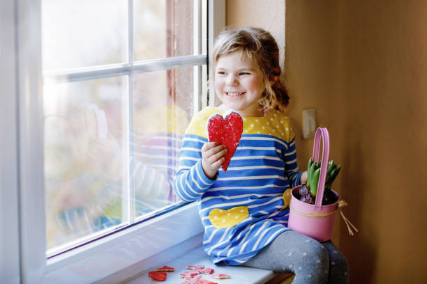 Little girl sitting by window with hyacinth flowers and hand-made heart. Happy child, indoors. Mother's day, valentine's day or birthday and spring concept. Little girl sitting by window with hyacinth flowers and hand-made heart. Happy child, indoors. Mother's day, valentine's day or birthday and spring concept hyacinth red stock pictures, royalty-free photos & images