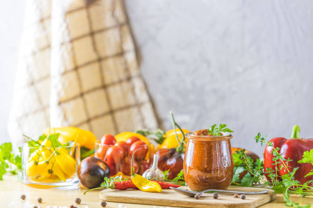 chutney di salsa di prugne calde in scatola naturale fai-da-te fatta in casa con peperoncino o tkemali in barattolo di vetro in piedi su un tavolo di legno con ingredienti. - chutney jar tomato preserved foto e immagini stock