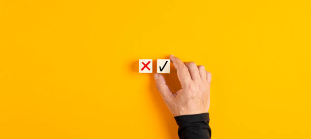 Right and wrong icons on wooden cubes with male hand choosing the right icon Right and wrong icons on wooden cubes with male hand choosing the right icon on yellow background. Approving, voting or right decision concept. oops stock pictures, royalty-free photos & images