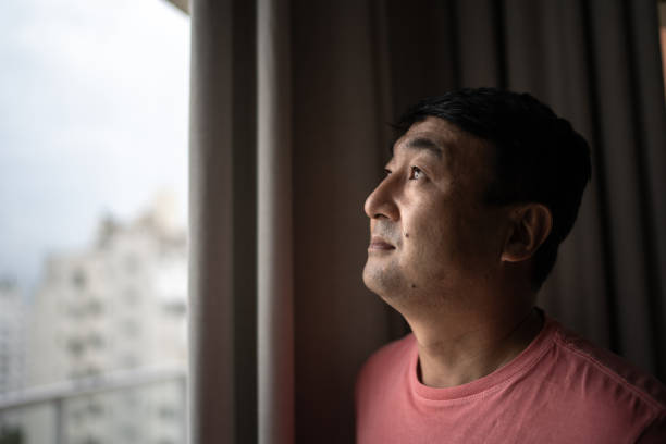 istock Mature man looking through window at home 1308830148