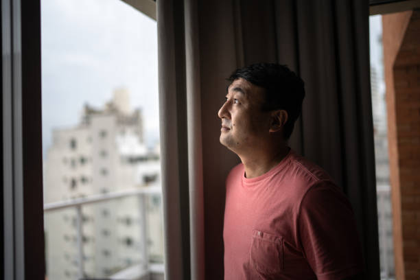 istock Mature man looking through window at home 1308830164