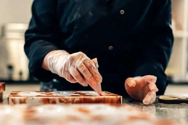 close up on hands of a pastry chef decorating white chocolates in an artisanal workshop