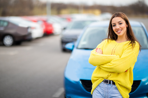 Smiling young women in yellow sweater looking at camera in front of few rent a car cars