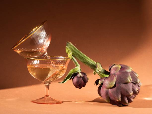 two champagne glasses with bubbles visible. there is an artichoke nearby. the photo was taken in close-up. party concept - artichoke vegetable macro close up imagens e fotografias de stock