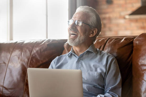 istock Smiling senior man use laptop in living room 1308834355
