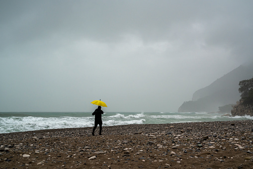 Lonely man walking on the beach on a rainy day