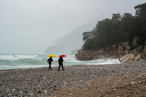 Two male friends walking on the beach on a rainy day
