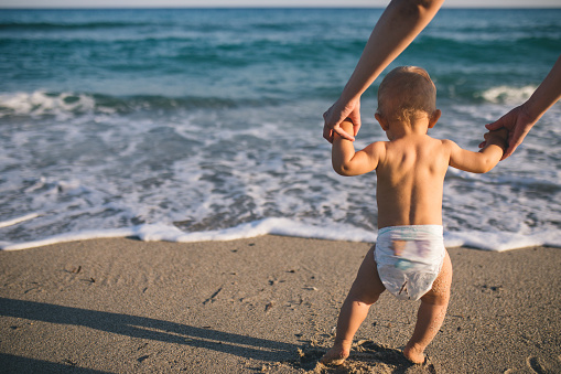 Mom helps to make the child's first steps on the beach