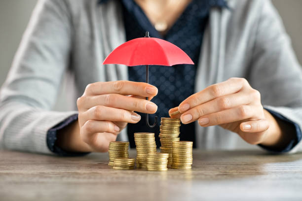 Hands protecting pile of coins with umbrella Young woman hands holding red umbrella over stacked coin on table. Female hand holding a small umbrella to protect heaps of coins while saving them. Financial security and savings protection concept. recession protection stock pictures, royalty-free photos & images