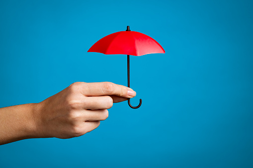 Female hand with small red umbrella isolated on blue background. Close up of woman hand holding mini umbrella against blue wall with copy space. Insurance, protection and security concept.