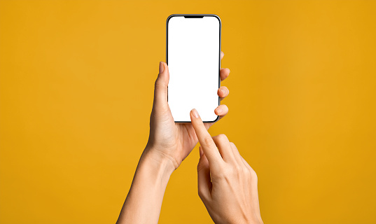 Close up of woman hand using smartphone isolated on orange wall. Female hands showing empty white screen of modern smart phone against vivid background. Businesswoman holding cellphone and unlocks it with her fingerprint.