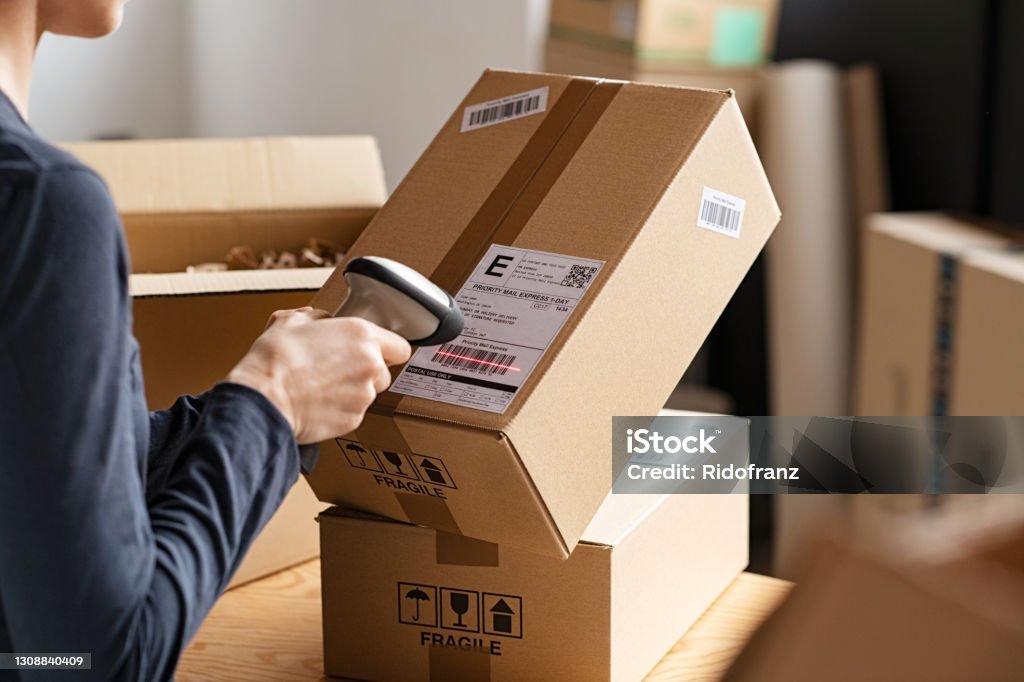 Scanning parcel barcode before shipment Hands of young woman scanning barcode on delivery parcel. Worker scan barcode of cardboard packages before delivery at storage. Woman working in factory warehouse reading and scanning labels on the boxes with bluetooth barcode scanner. Delivering Stock Photo