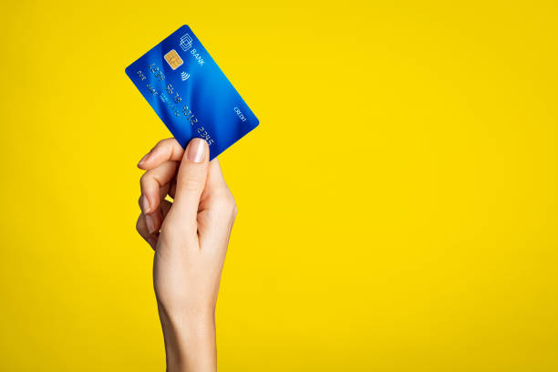 Female hand holding bank credit card Close up of woman hand showing credit card on yellow background. Detail of female hand holding bank credit card against yellow wall with arm raised. Young woman showing creditcard with copy space. credit card purchase stock pictures, royalty-free photos & images