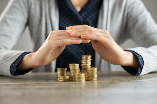 Close up of woman hands covering coins on table. Woman protecting and securing money and savings on wooden table. Safety of savings, investment and insurance concept.