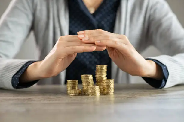 Close up of woman hands covering coins on table. Woman protecting and securing money and savings on wooden table. Safety of savings, investment and insurance concept.