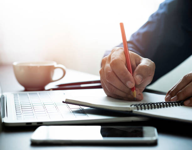 istock Close-up of man hand using writing pencil memo on notebook paper or letter, diary on table desk office. Workplace for student, writer with copy space. business working and learning education concept. 1308848529