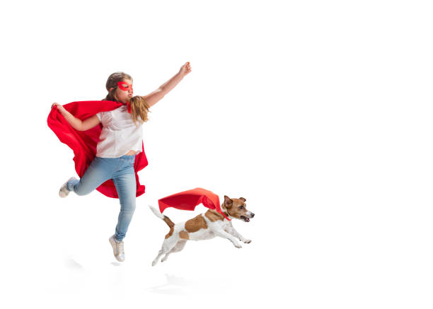 Child pretending to be a superhero with her super dog isolated on white studio background Child pretending to be a superhero with her super dog in red coats isolated on white studio background. Dreams, emotions, pet's love and friendship, motivation concept. Powerful together. Copyspace. cape garment stock pictures, royalty-free photos & images
