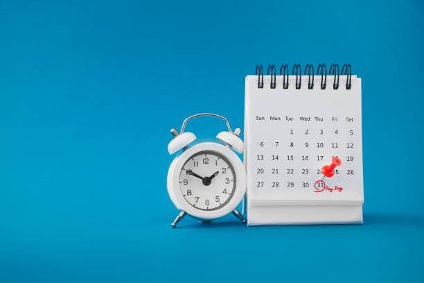 red thumbtack pin on the last day  of month with circle and pay day word near white analog clock on grunge blue background for business and finance concept stock photo
