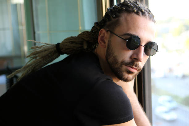 attraktives, junges blondes bärtiges männliches model mit kombination aus zöpfen und dreadlocks, die auf dem balkon posieren. - young men men blond hair attractive male stock-fotos und bilder