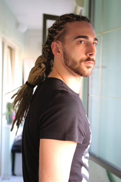 attraktives, junges blondes bärtiges männliches model mit kombination aus zöpfen und dreadlocks, die auf dem balkon posieren. - young men men blond hair attractive male stock-fotos und bilder