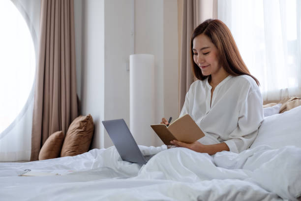 istock A beautiful young asian woman using laptop computer and working on paperwork while sitting on bed at home 1308859976
