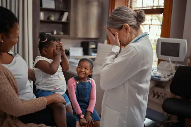 Shot of a doctor playing peekaboo with an adorable little girl while doing a consult