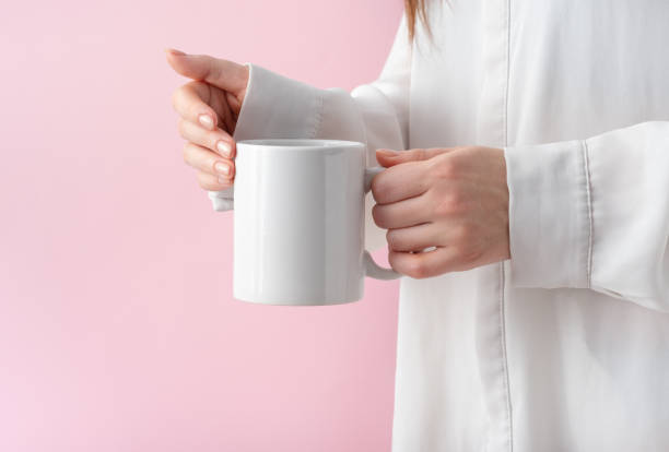 istock mockup white coffe cup or mug in female hands on pink background with copy space. Blank template for your design, branding, business. Real photo. Woman in shirt casual style 1308864250